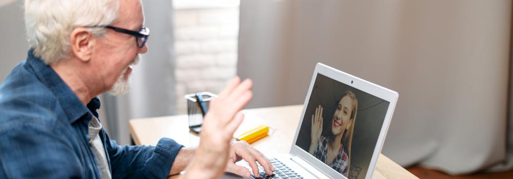 elder male on laptop waving