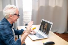 elder male on laptop waving